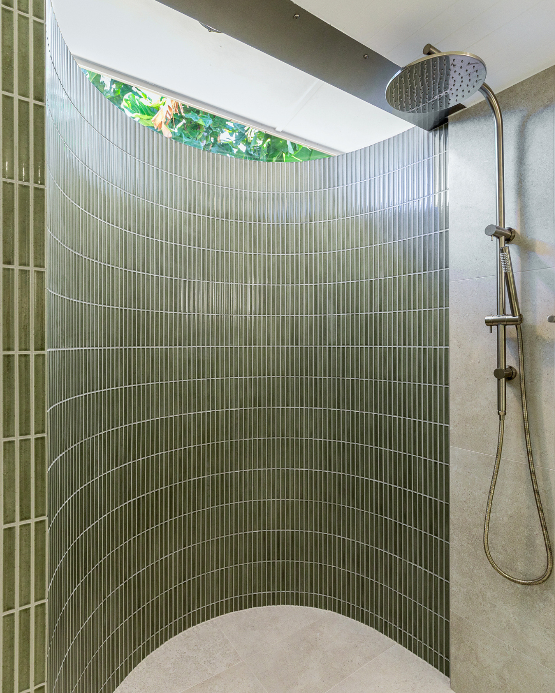 Curved shower wall clad in green Blade Kit Kat Forest mosaic under a skylight